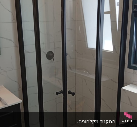 מקלחון זכוכית עם מסגרת שחורה וכלים על הרצפה